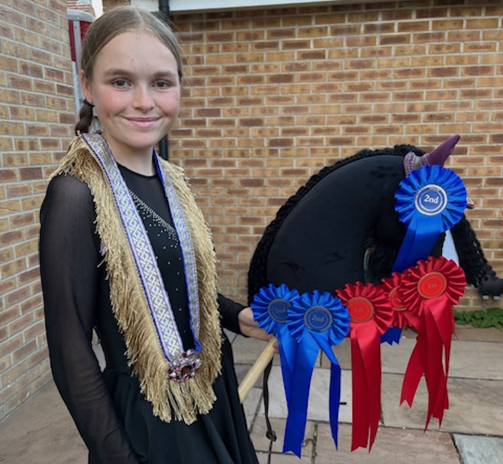 Young girl with rosettes and a sash on her black hobby horse