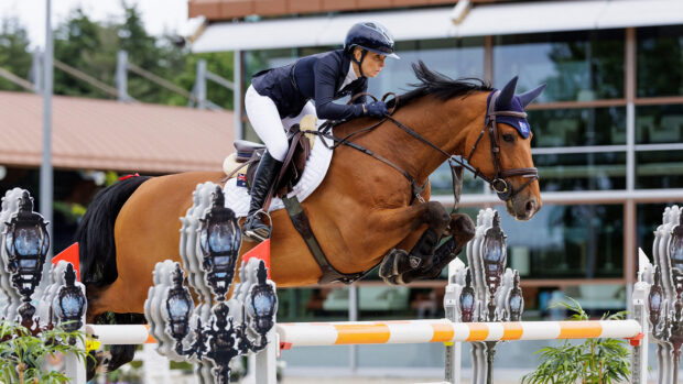 Australian rider Edwina Tops-Alexander clears a large oxer of white and yellow poles riding Fellow Castlefield