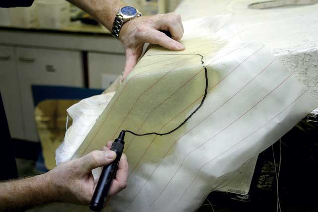 3: Once cured, the mould is transferred to the damaged area, and positioned over the hole. A pen line is marked around the damage, allowing about an inch of overlap. (The hole can be clearly seen through the cloth.)