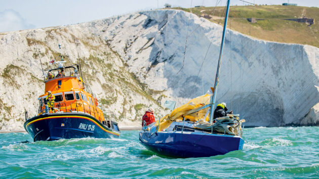 An RNLI lifeboat rescuing a yacht after boat engine failure close to cliffs