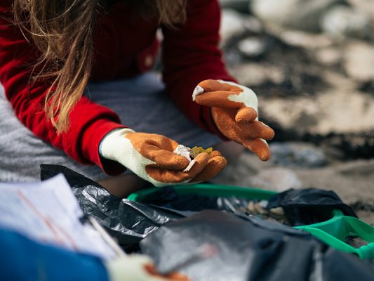 A woman wearing gloves picking up plastic on a beach