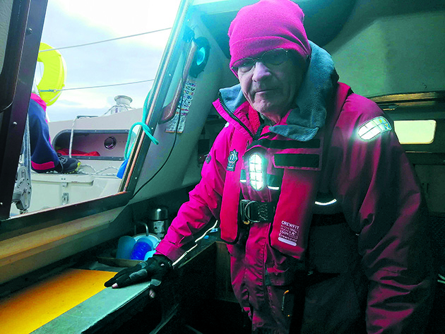 A man wearing a red hat, lifejacket and jacket standing on a boat