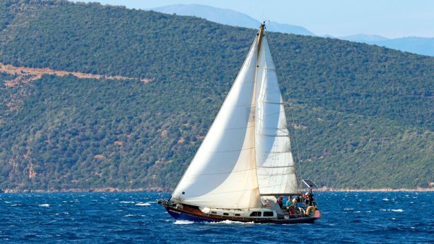 A boat with white sails sailing in the Northern Sporades in Greece