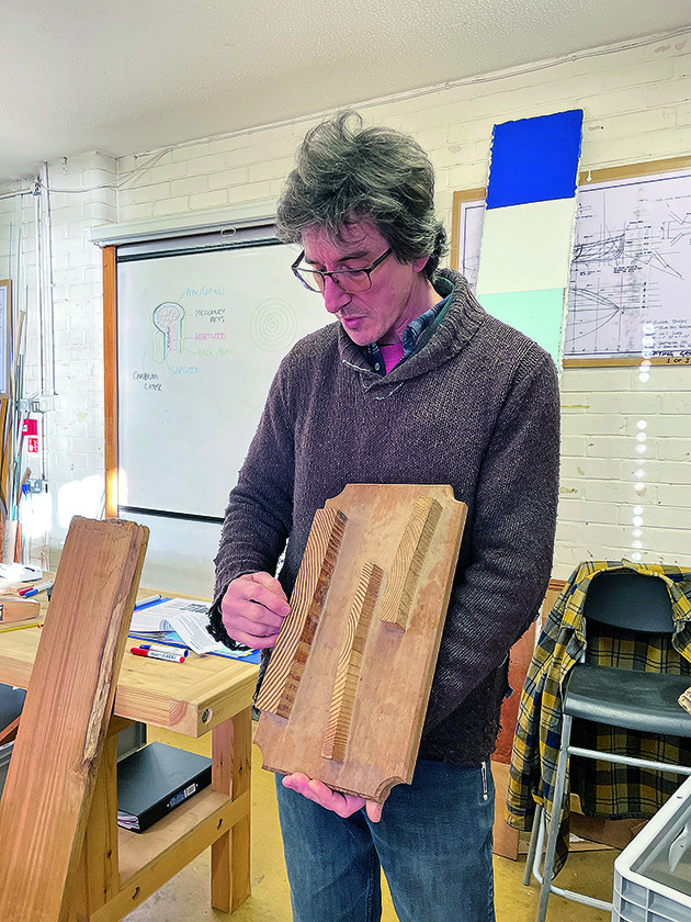 a man holding a piece of timber while teaching how to become a boat builder course