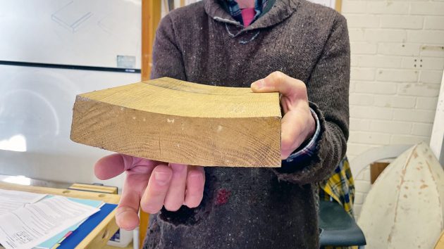 A man holding a piece of wood which has a bow in it