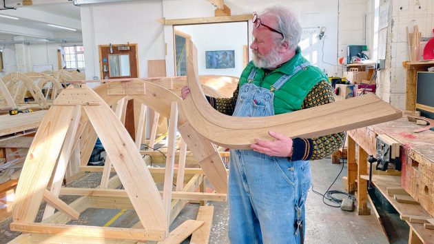 A man holding a piece of wood during a how to become a boat builder course