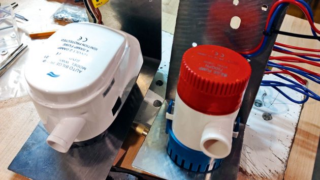 A white automatic bilge pump and a red and white manual bilge pump on a work bench