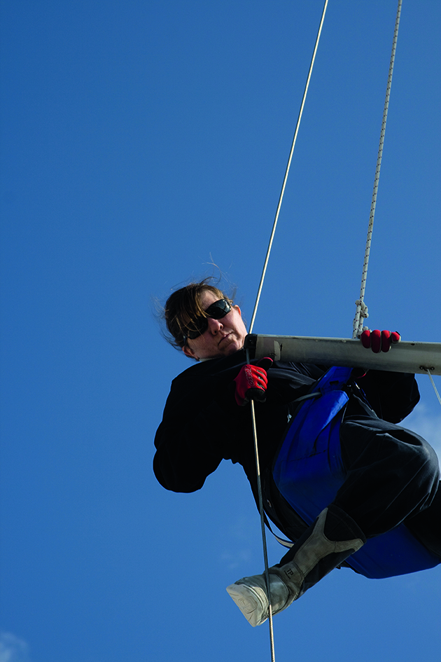 A woman up a mast performing a rig check on a yacht