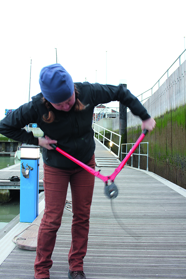 A woman holding a pair of heavy-duty cutters standing on a pontoon testing them in case of a dismasting