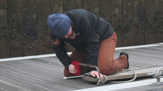 A woman using a hack saw to cut through metal to see what would work best in a dismasting