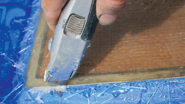 A knife being used to trim laminate from a piece of oak