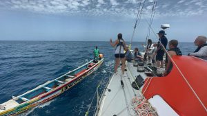 A man on a 20ft canoe approaching the crew of a 55ft yacht, Outlaw at sea