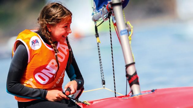 A girl wearing an orange tabard sailing in a small boat