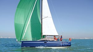 A yacht, made out of plywood, sailing with a blue hull and green and white sails