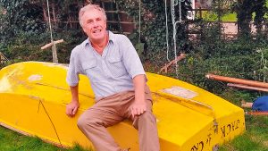 Sandy Mackinnon sitting on the yellow wooden mirror dinghy, Jack de Crow