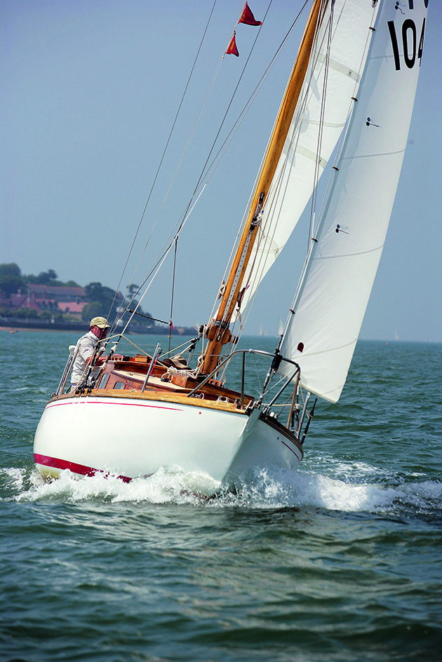 A boat with a white hull and a wooden mast with white sails