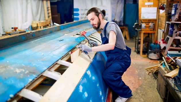 A man working with boat woods to make repairs to a boat