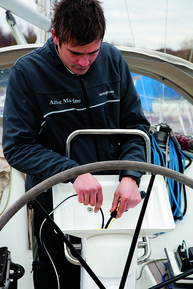 A man feeding electrical cabling through a pedestal during tiller to wheel conversion on a yacht