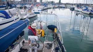 A man wearing a hat reversing a long keel sailboat in a marina