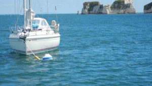 A yacht on the Studland eco moorings buoys with Old Harry Rocks behind