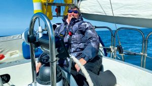 A woman sailing with limited mobility smiling wearing a blue coat while sailing