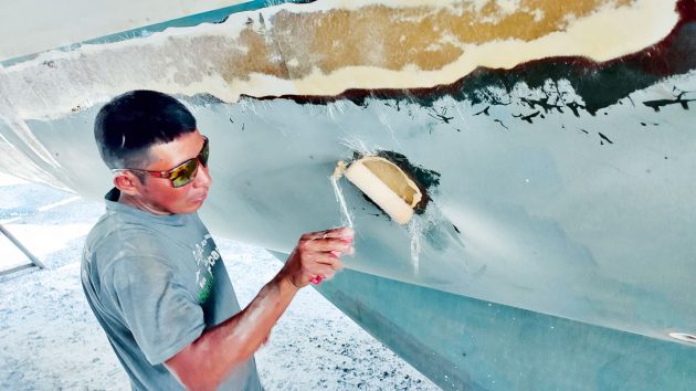 A man using a roller to soak a hull of the boat in laminate while carrying out boat fibreglass repair