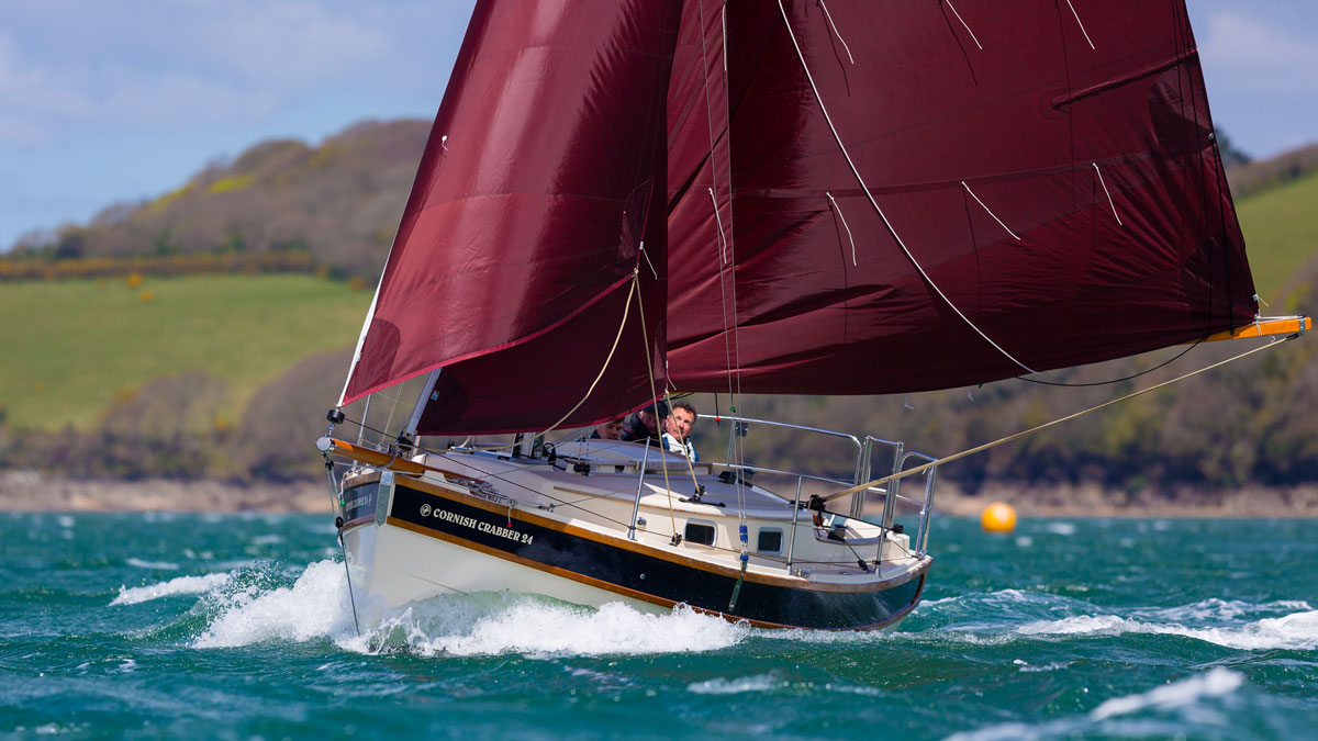 A Cornish Crabbers boat, the Crabber 26 being sailed by a man near the coast
