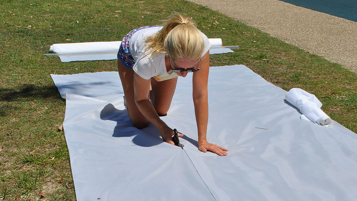 A woman cutting out fabric on a lawn for a spinnaker snuffer
