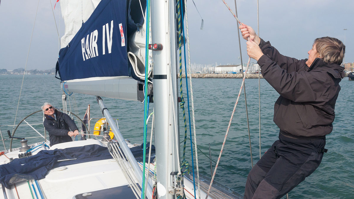 A woman hoisting a mainsail of a yacht at the mast