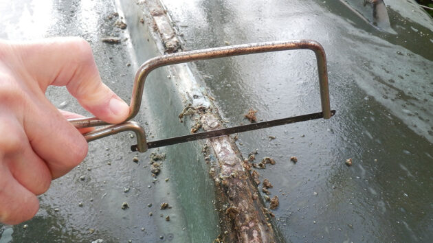 A man using a hack saw to cut out screwheads from a keel band on a boat