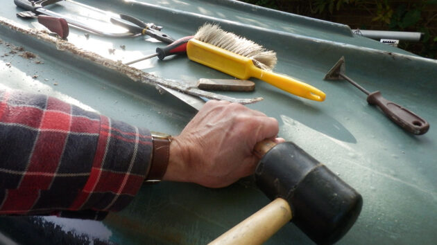 A man using a hammer to remove keel band from a boat