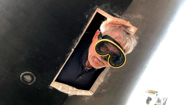 A man sticking his head out of a hole on a boat which has been cut to fit a bow thruster