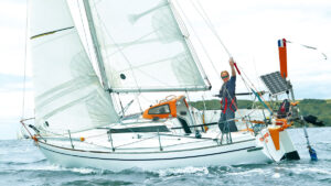 A small yacht heading offshore with a man waving on board