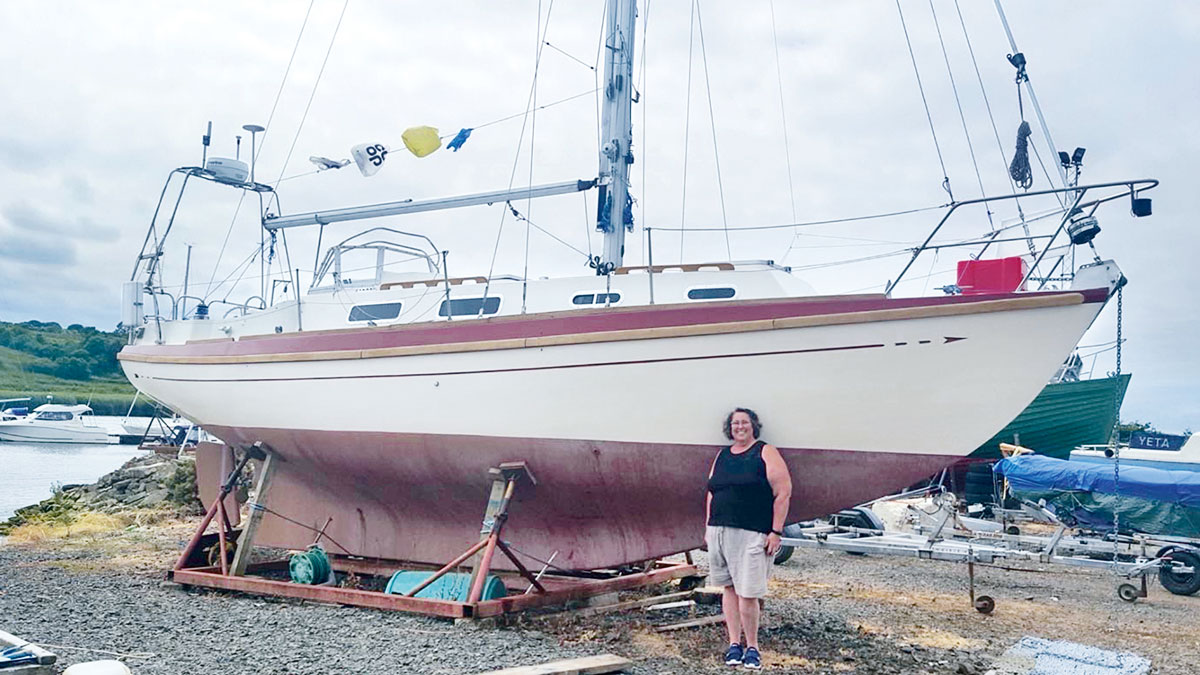 A woman standing by a boat that she bought for her dream voyage