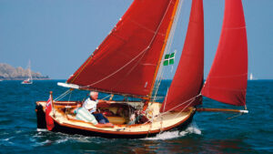 A man sailing an Oysterman 16 boat with red sails