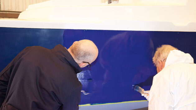 Two men applying blue paint to a boat
