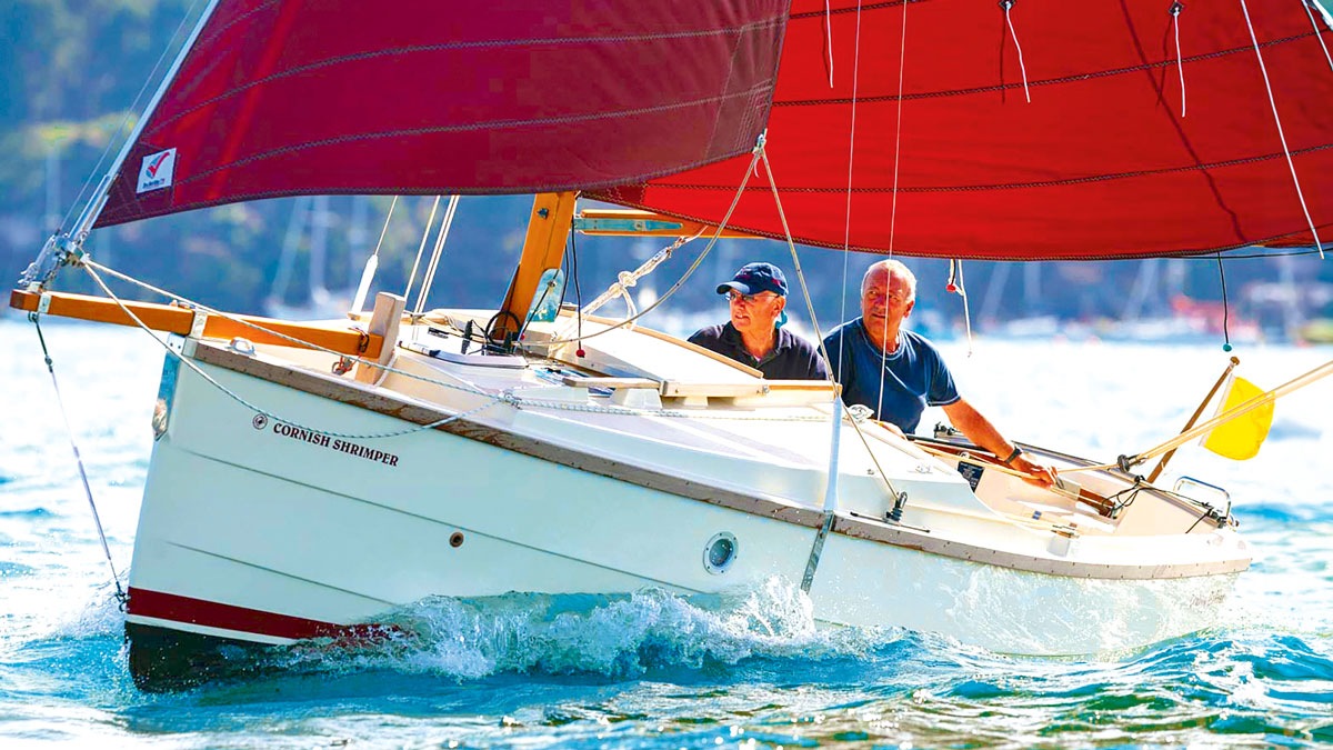 Two men sailing a Cornish Shrimper 19 boat with a red sail