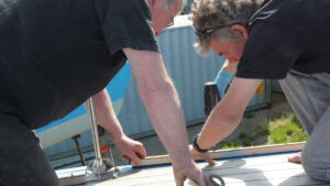 Two men using a drill to fit a new toerail to a yacht