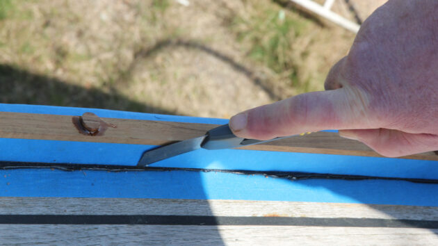 A man using a craft knife to trim off cured sealant on a boat