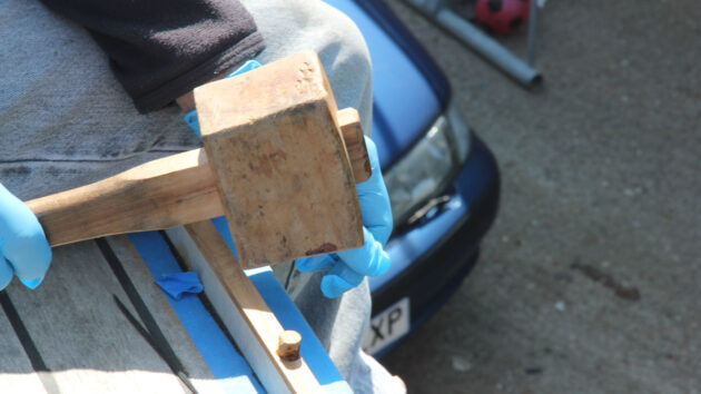 a wooden mallet being used to install plugs into a toerail on a boat