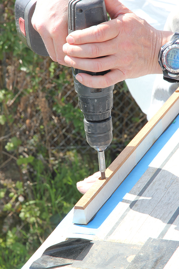A man using a drill to fit a new toerail on a boat