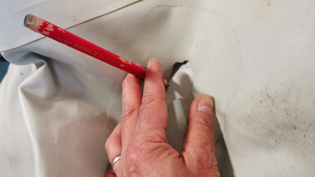 A man with a pencil while carrying out inflatable dinghy repairs