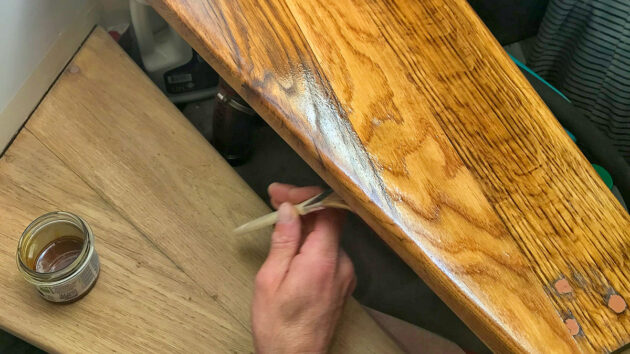 A person painting wood oil on steps on a boat