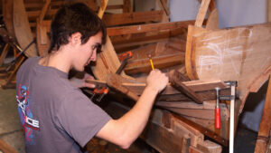 A man repairing a hull plank on a clinker-built boat