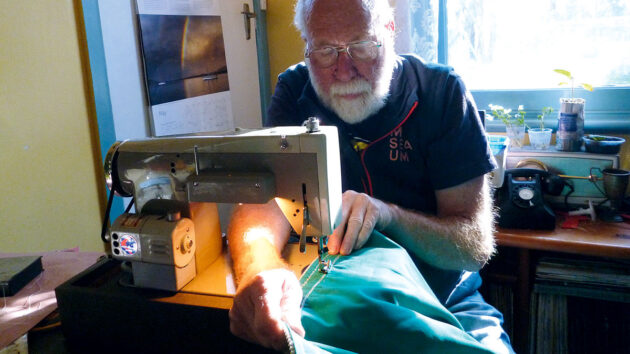 A man using a sewing machine to make repairs to a sail cover