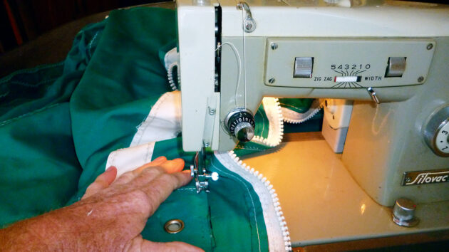 A man making repairs to a boat sail cover with a sewing machine