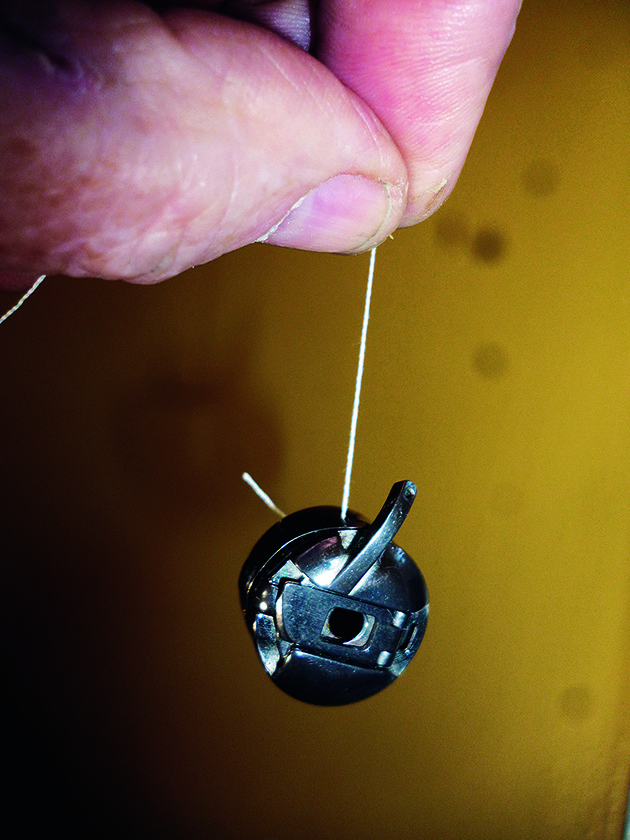 A man checking the tension of a sewing machine bobbin