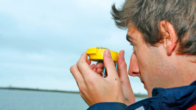 A man on a boat taking a bearing with a compass