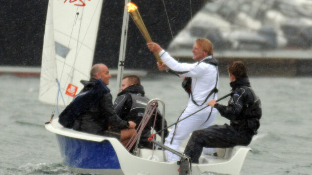 a man carrying a flame in a boat at the start of the London 2012 olympics. Many sailors taking part had started at Royal Yachting Association training centres