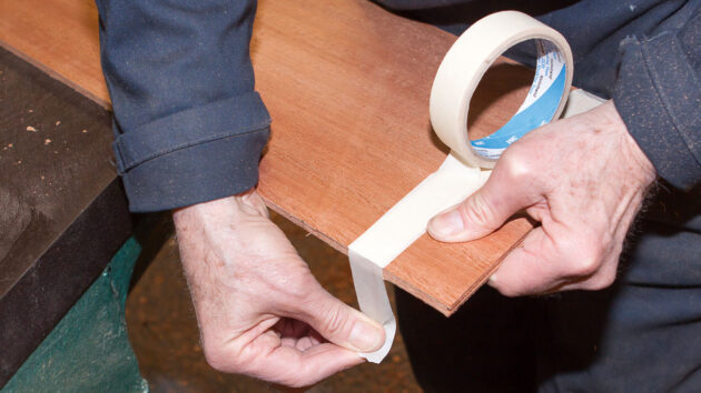 A man applying masking tape on wood